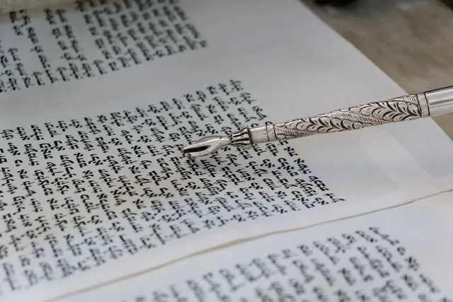 A silver yad resting on the open columns of a Torah scroll